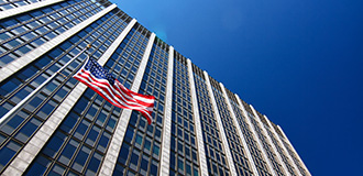 high-rise building against a blue sky, with a US flag in front of the building