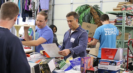 Older woman with face mask going through clothing donations and man and woman cooking something in pot behind her