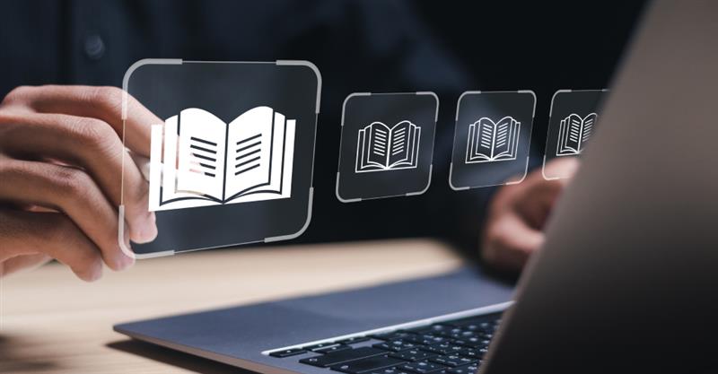 A person focused on a laptop, with various book icons displayed on the screen, symbolizing learning and knowledge.