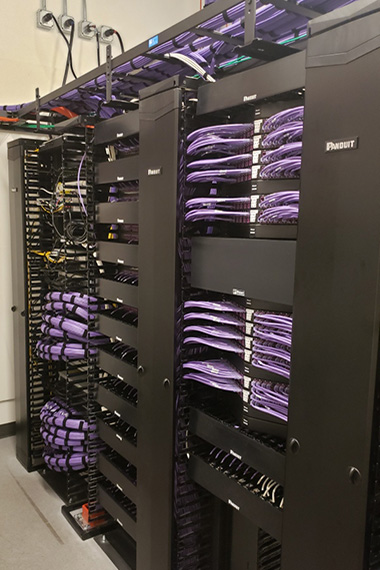 Black Panduit racks and cable managers built out with purple category 6a cabling, patch cords, patch panels, and jacks, in a telecommunications room