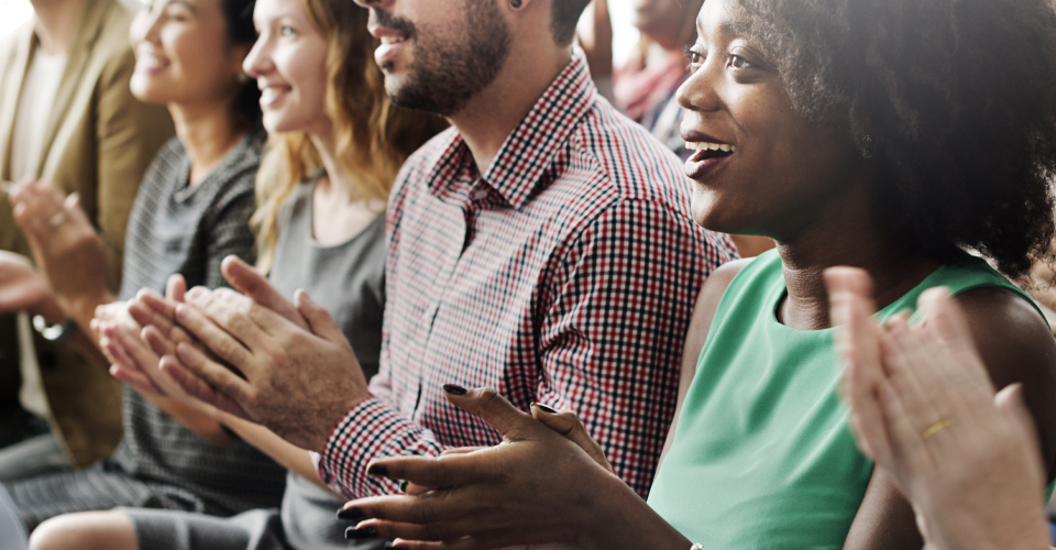  A diverse crowd of people enthusiastically clapping together, showcasing unity and celebration in a lively atmosphere.