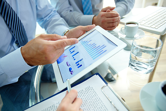 Hands pointing at graphs on an electronic tablet at a conference room table