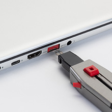 A laptop computer with a red physical port blocker installed, along with the tool that is used to remove the device