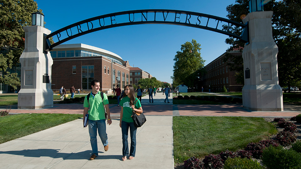 Students walking on campus under an arched sign that says Purdue University